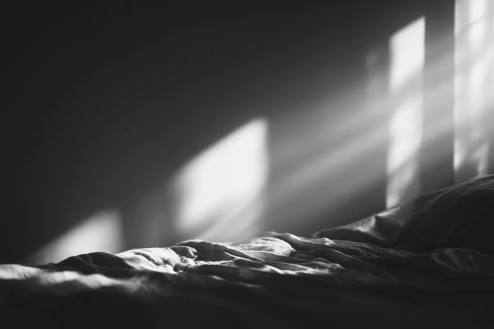 An empty bed in a bare room in soft grey morning light.