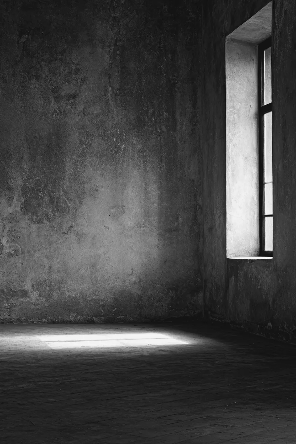 An empty room with a high window throwing a shaft of light onto a bare floor.