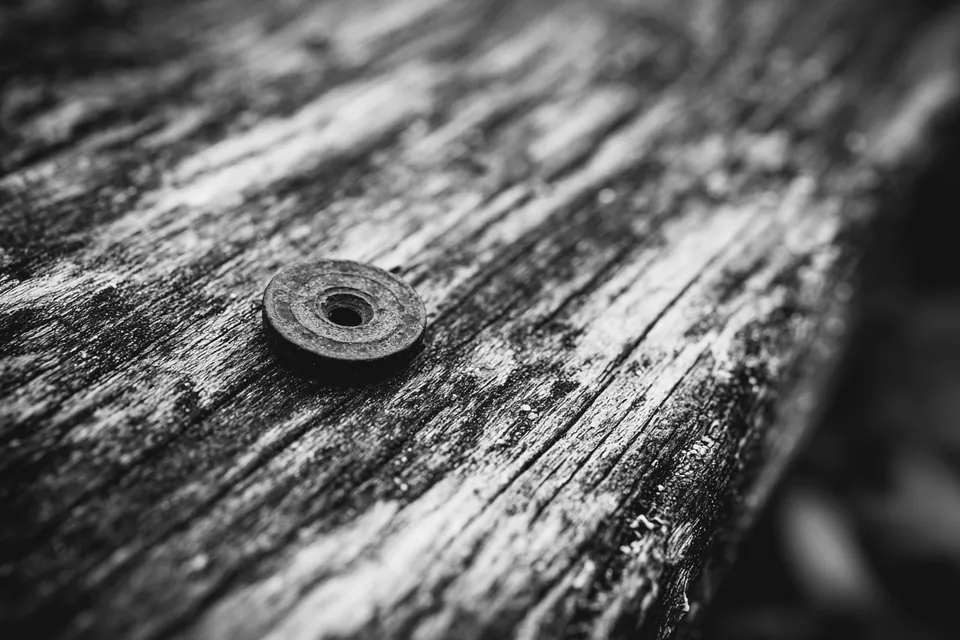 A single darkened brass washer resting on bare weathered wood.